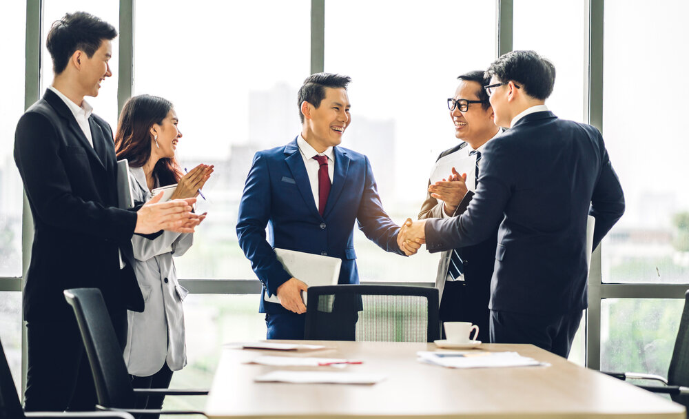 Image two asian business partners in elegant suit successful handshake together in front of group of casual business clapping hands in modern office.Partnership approval and thanks gesture concept